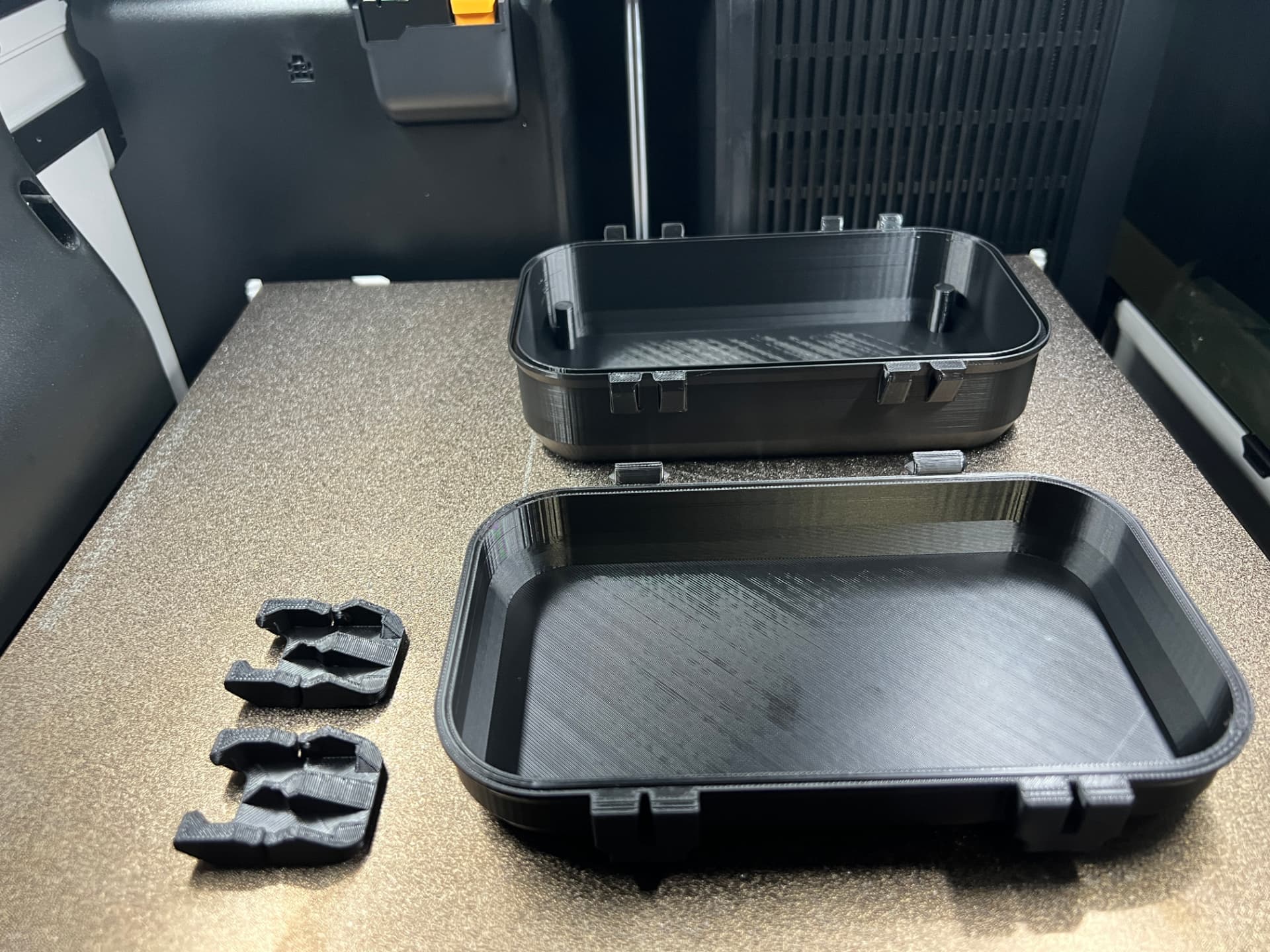 Finished black 3D printed enclosures and clips on a build plate